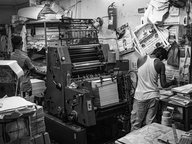 Workers at a sheet-fed offset printing press in a print shop